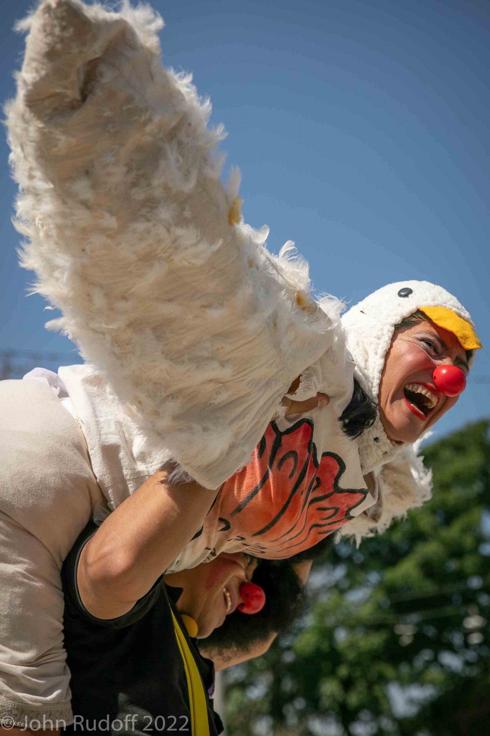 Clown in chicken costume being lifted up by another clown