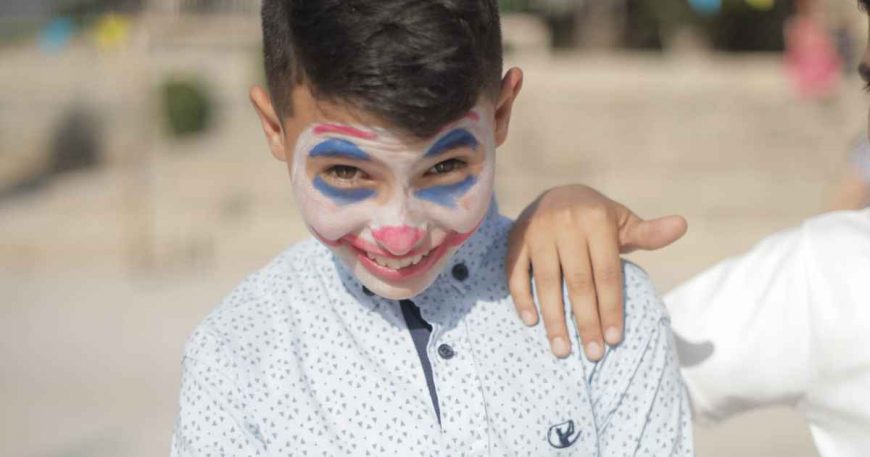 A boy about 12 years old wears traditional clown makeup.