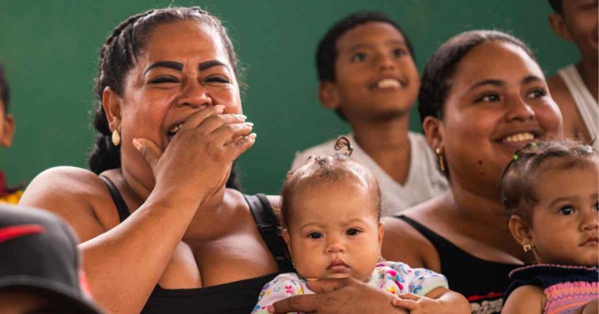 Young mothers with their babies laugh at a clown show in Ecuador.