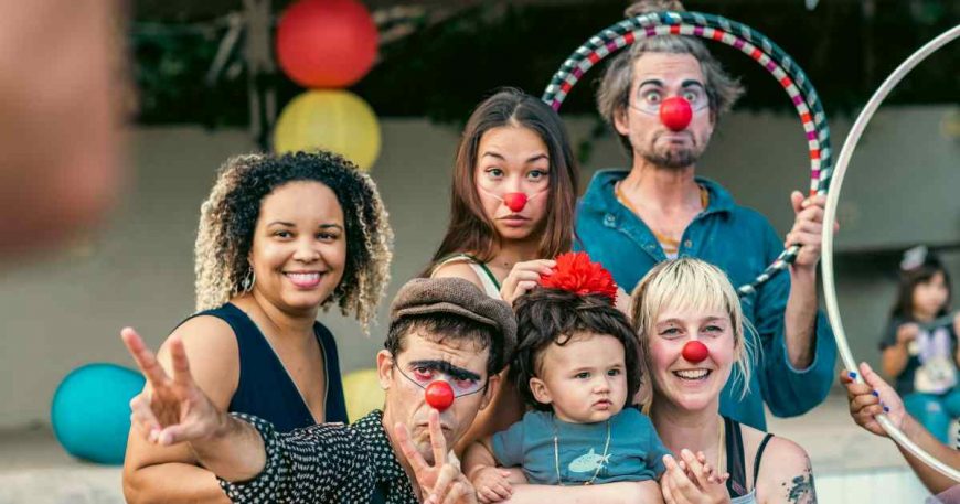 Portrait of four clowns with a woman and a baby with a funny wig and flower.