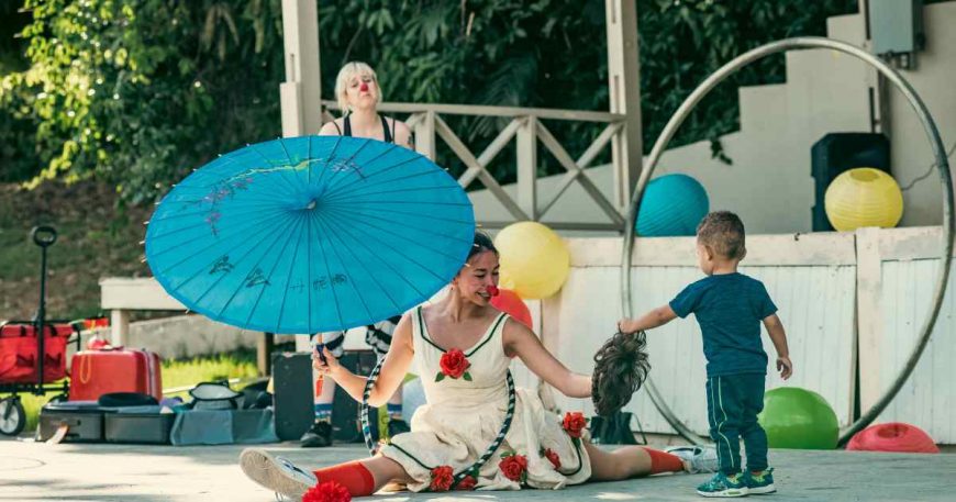 A clown in a dress and with a blue umbrella performs for children in Puerto Rico.