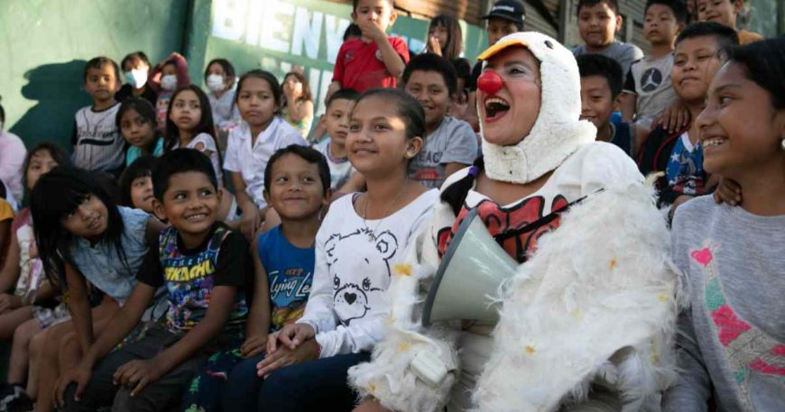a clown dressed as a chicken sits with kids in a clown show audience