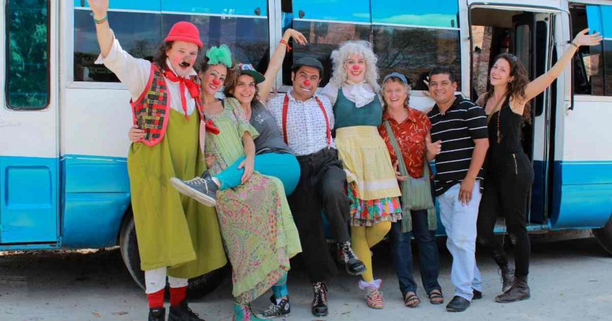 A group of clowns and friends posing in front of bus