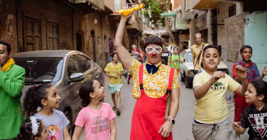 clown in a yellow shirt and red pants leads a group of children through the streets in Cairo