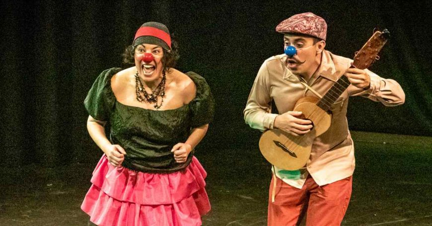 Two clowns on stage engaged in a song; one clown plays a guitar.