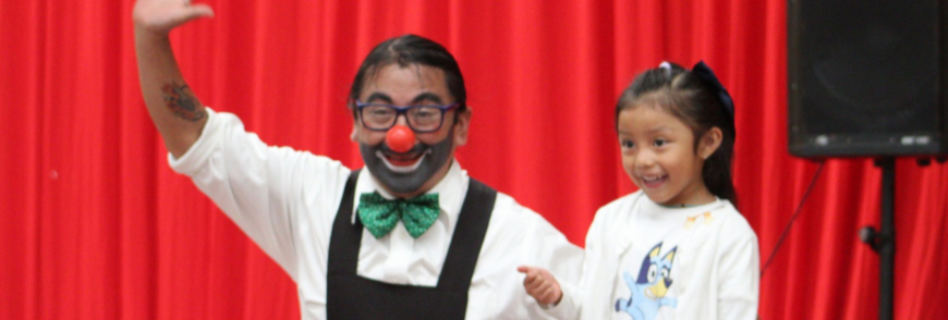 A clown kneeling next to small child with a red curtain backdrop.