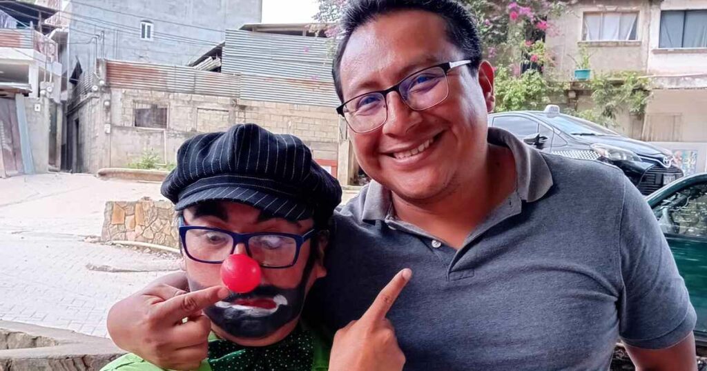 A clown points to a man and the man points to the clown's nose as they embrace and pose for a photo at a clown show.