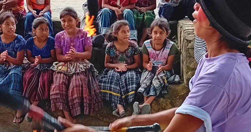 A woman juggling fire in front of a row of Indigenous girls in Guatemala.