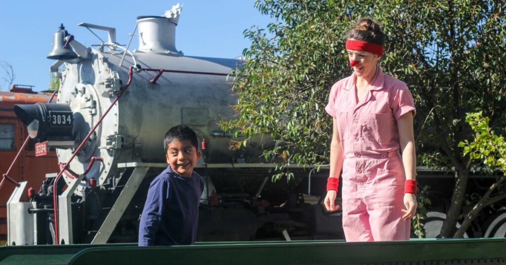 A boy joins a clown on stage in front of a train.